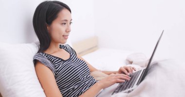 Onun köpeği ile dizüstü bilgisayar üzerinde çalışan ve yatağın üstüne oturan kadın 