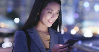 Gece şehirde akıllı telefon kullanan bir kadın. 