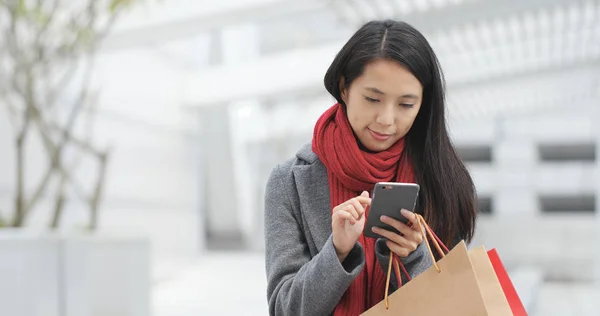 Kobieta Pomocą Smartfona Przytrzymując Torby Zakupy — Zdjęcie stockowe