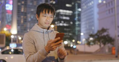 Geceleri şehirde akıllı telefon kullanan bir adam. 