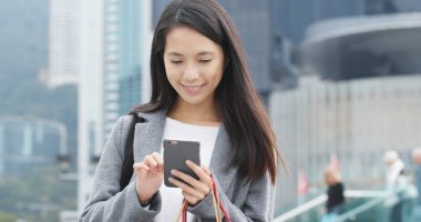 Cep telefonu kullaranarak ve alışveriş çantası tutan kadın 