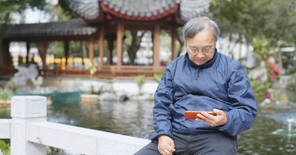 Asian old man using mobile phone and sitting at chinese garden