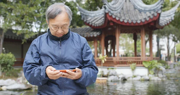Ασιατικές Ανώτερος Άνθρωπος Βλέποντας Στο Κινητό Τηλέφωνο Στην Κινεζική Κήπο — Φωτογραφία Αρχείου