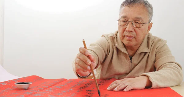 Chinese man writing chinese calligraphy on red paper