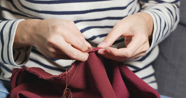 Woman Sews with a needle and thread at home 