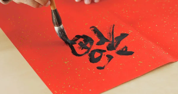 Writing Chinese calligraphy on red paper, words meaning luck