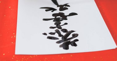 Writing Chinese calligraphy on write paper with phrase meaning may you have a prosperous New Year  clipart