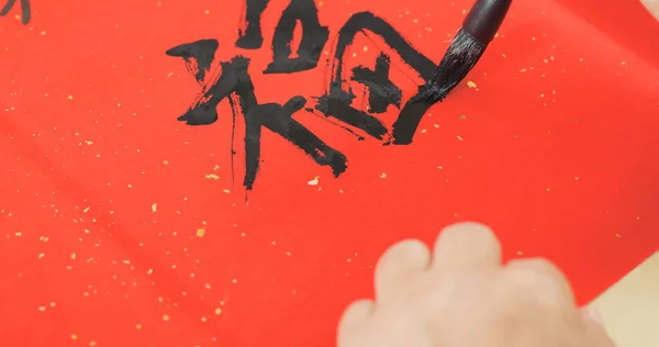 Writing Chinese calligraphy on red paper, words meaning luck for lunar new year