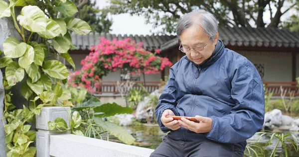 Old man watching on smartphone inside beautiful Chinese garden