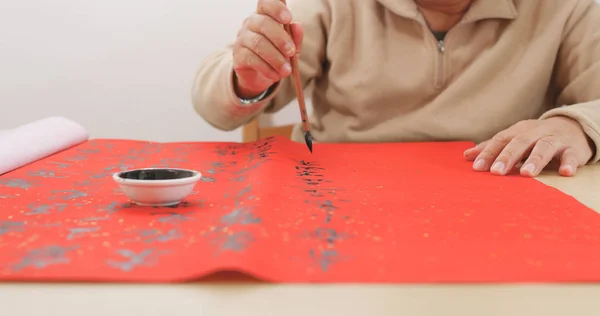 Old man writing Chinese calligraphy on red paper