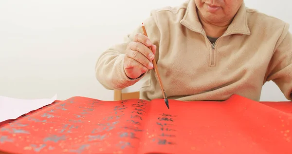 Old man writing chinese calligraphy on red paper