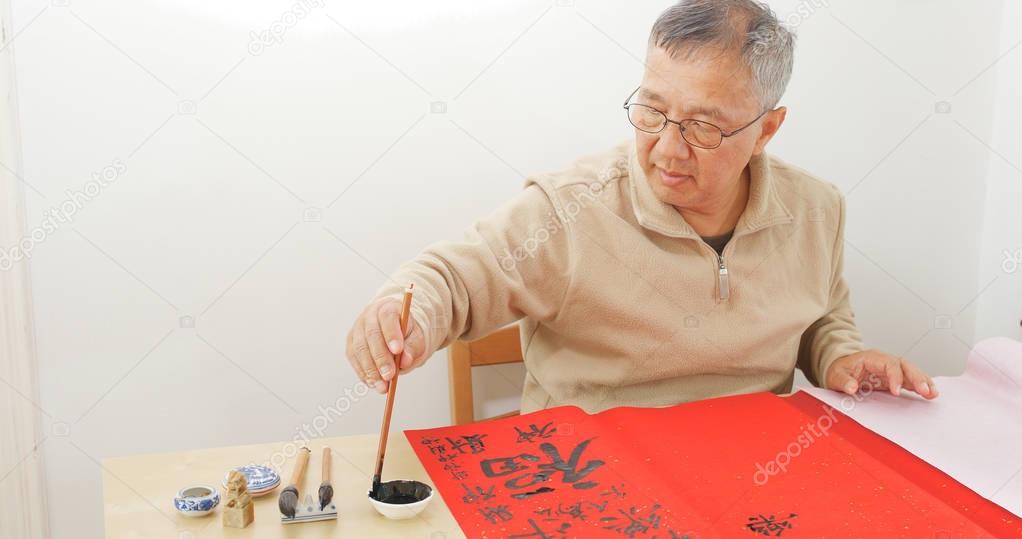 Old man writing Chinese calligraphy on red paper for lunar new year 
