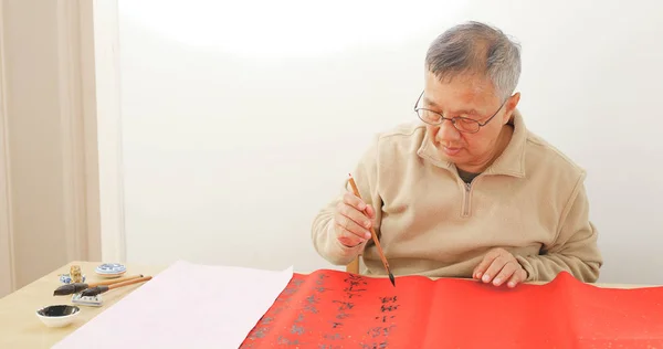 Asian man writing chinese calligraphy on red paper