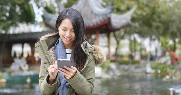 Young woman using mobile phone, sending sms and reply group chat on app at China, Chinese pavilion garden