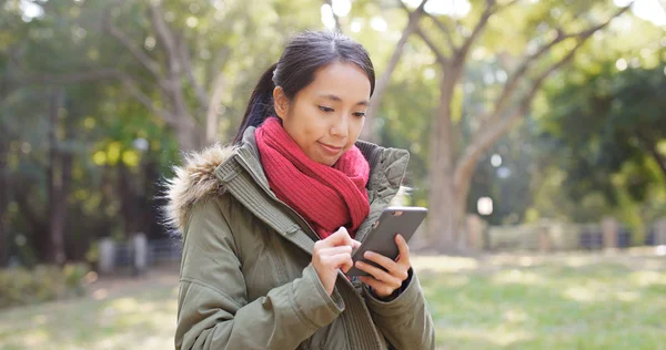 都市公園に立っていると屋外でスマート フォンを使用して冬のジャケットを着ている女性 — ストック写真