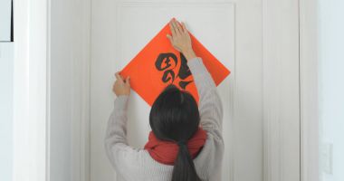 Woman sticking chinese calligraphy on the door for lunar new year clipart
