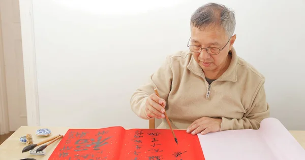 Old man writing Chinese calligraphy on red pape
