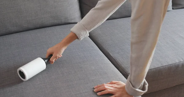 Housewife with sticky roller cleaning sofa