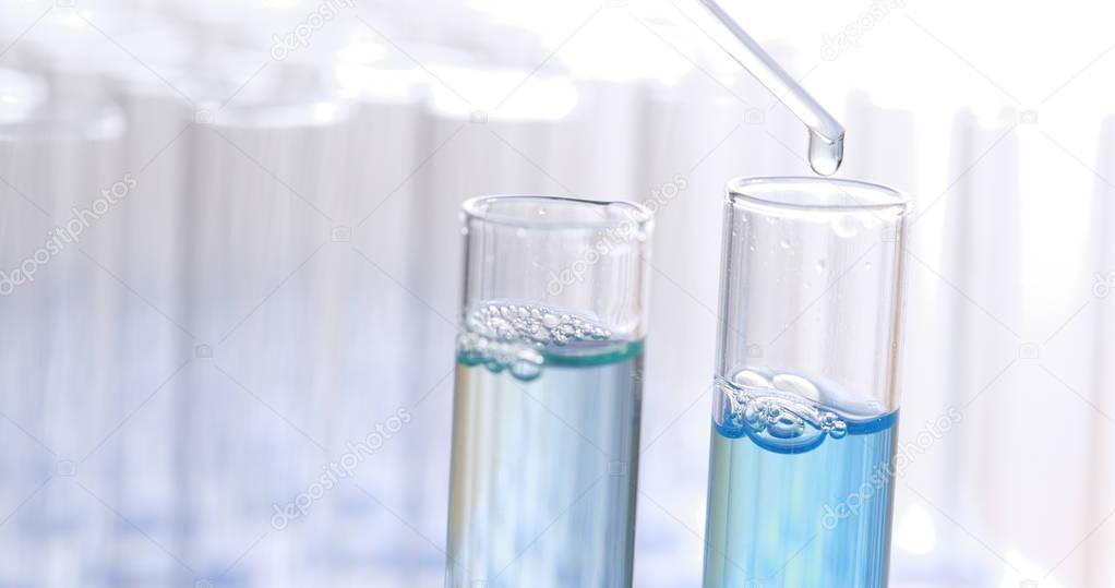Pipette drips blue chemicals into a test tubes 