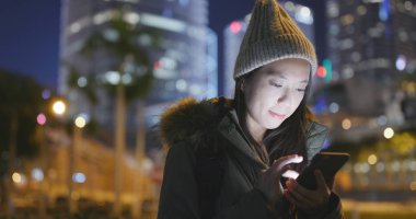 Kış ceket giyiyor ve geceleri cep telefonu kullanan kadın