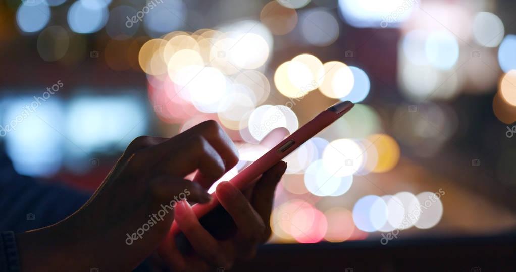 Woman working on mobile phone over city traffic at night 