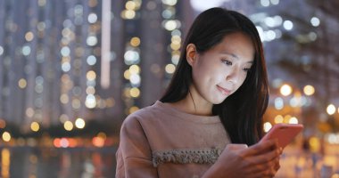 Gece şehirde akıllı telefon kullanan bir kadın. 