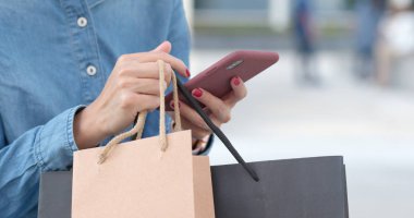 Alışveriş torbaları holding ile alışveriş için cep telefonu kullanan kadın 