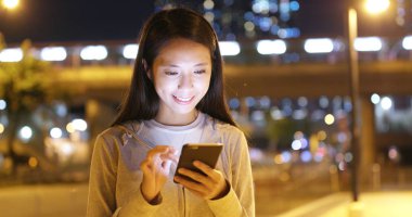 Smartphone şehirde geceleri kullanan genç kadın 