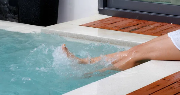 Femme assis sur le côté de la piscine et secouer les jambes — Photo