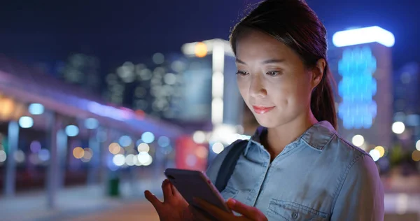 Mulher olha para o telefone celular na cidade à noite — Fotografia de Stock