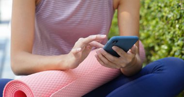 Dışarıda yoga minderiyle cep telefonu kullanan bir kadın.
