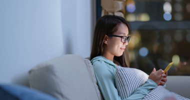 Gözlüklü ve akşam evde cep telefonu kullanan bir kadın.