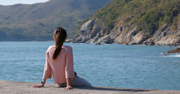 Mulher senta-se à beira-mar e olha para o mar — Fotografia de Stock