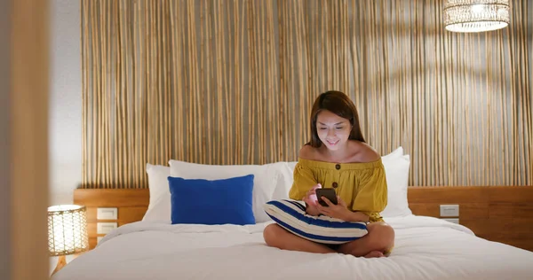 女性は携帯電話でゲームをプレイし ベッドの上に座る — ストック写真