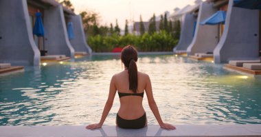 Kadın gün batımında havuzda oturur.