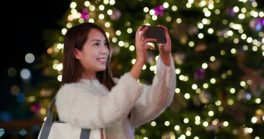 Kadın Noel ağacı süslemesinde fotoğraf çekiyor.