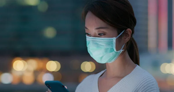 Woman wear medical face mask and use of mobile phone in city at sunset