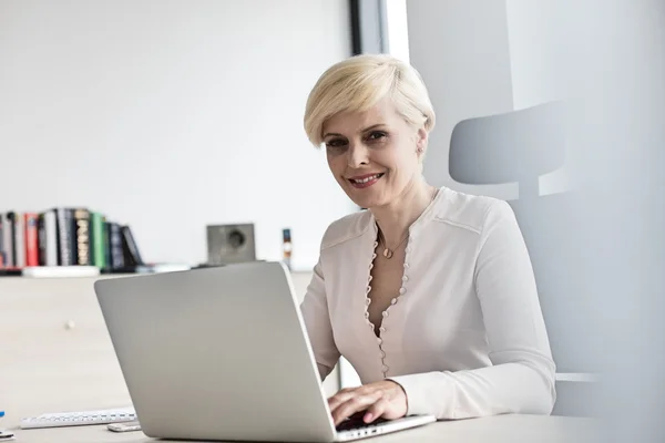 Uśmiechnięta kobieta korzysta z laptopa w biurze — Zdjęcie stockowe