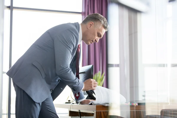 Mature businessman reading book at desk in office — Stock Photo, Image