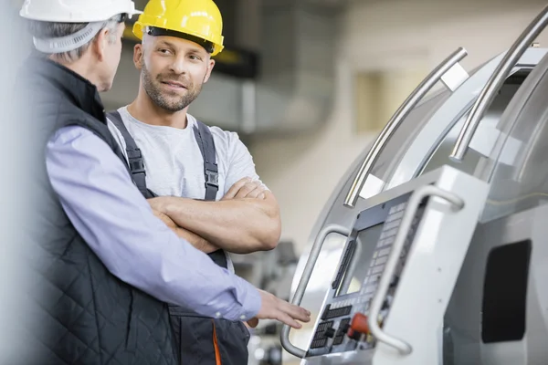 Worker having discussion with colleague by machinery Royalty Free Stock Photos