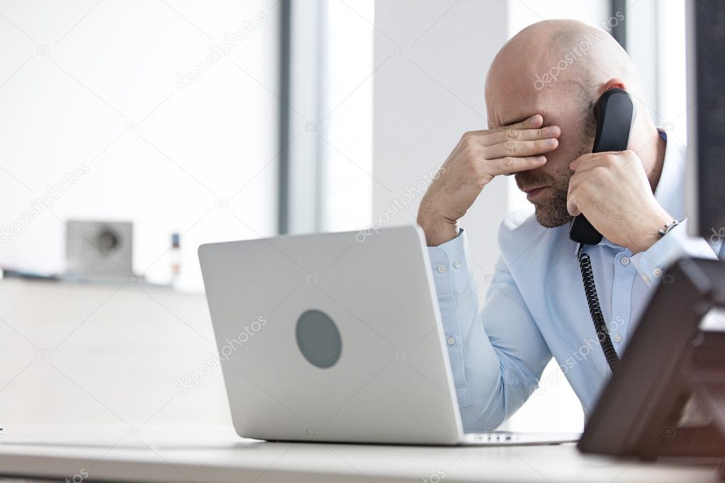 Tired businessman using telephone in office 