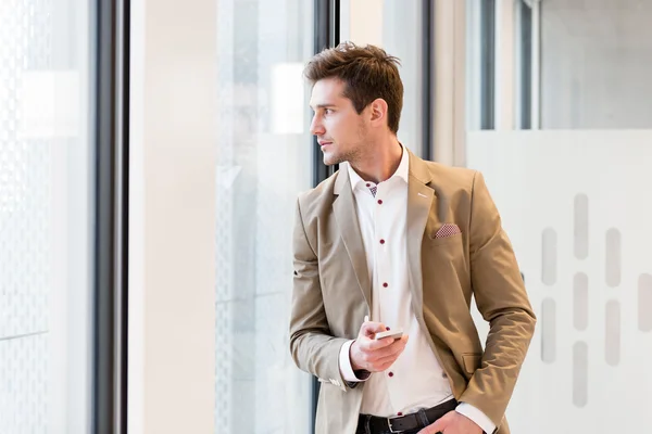 Young businessman looking through office window — Stock Photo, Image