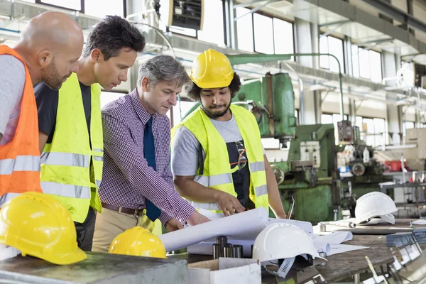 Toezichthouder met werknemers bespreken over blauwdrukken — Stockfoto