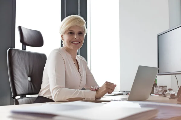 Mujer de negocios sonriente sentada en el escritorio en la oficina —  Fotos de Stock