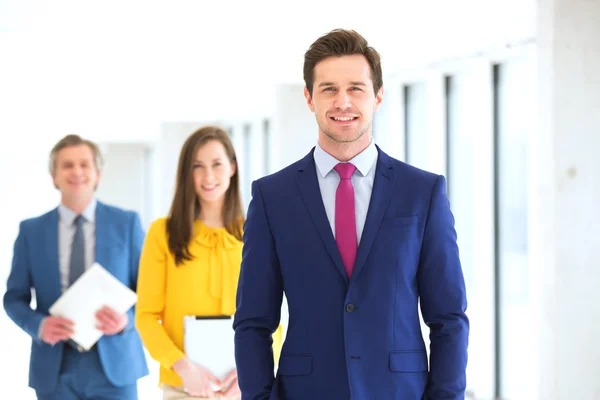 Hombre de negocios seguro con el equipo en el fondo en la oficina — Foto de Stock