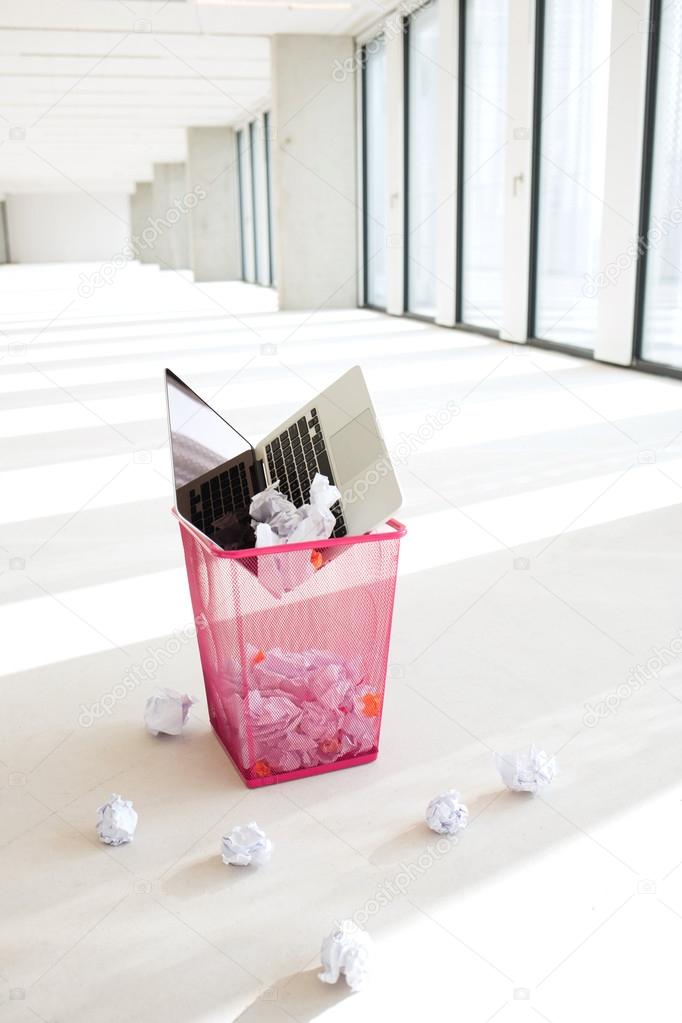 Laptop and crumpled papers in basket at office