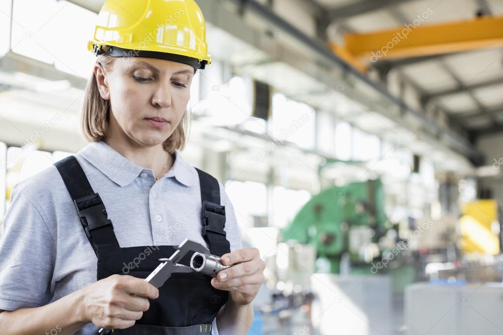 female worker measuring metal with caliper in industry 