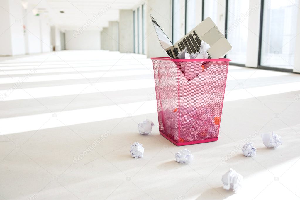 Laptop and crumpled papers in basket at office