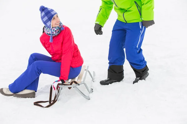 Frau sitzt auf Schlitten und schaut Mann an — Stockfoto