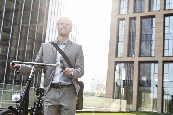Вдумчивый бизнесмен, стоящий с велосипедом — стоковое фото